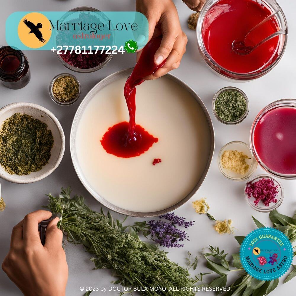 Image shows a person carefully pouring melted red wax into a candle mold with herbs and essential oils on the table